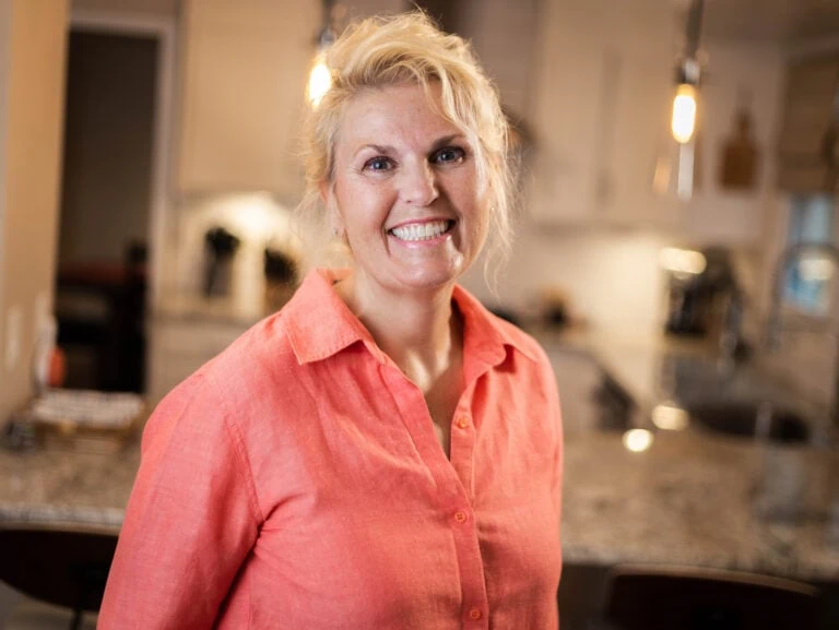 woman with blonde hair and orange shirt smiling at camera